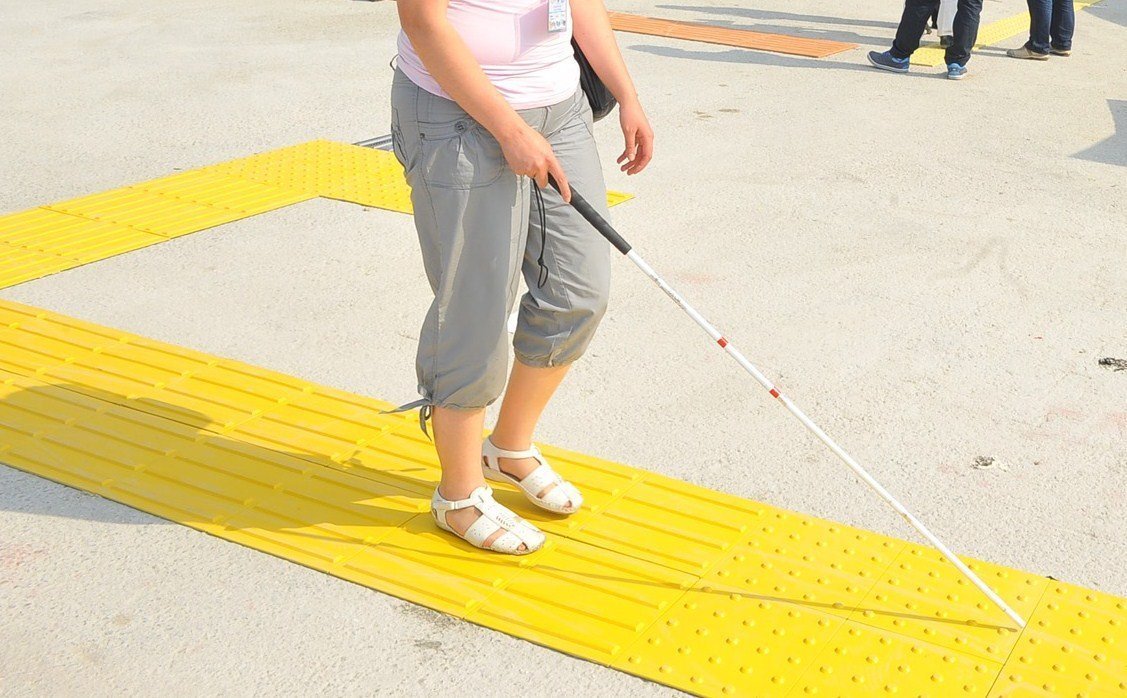 İstanbul dış mekan projesinde Rednasis sarı hissedilebilir yüzey (kılavuz iz ve uyarıcı yüzey) üzerinde beyaz bastonla güvenle ilerleyen görme engelli birey.